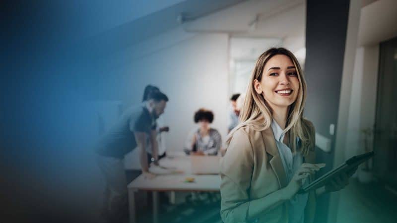 Eine junge Frau mit Tablet in der Hand steht in einem Büro.