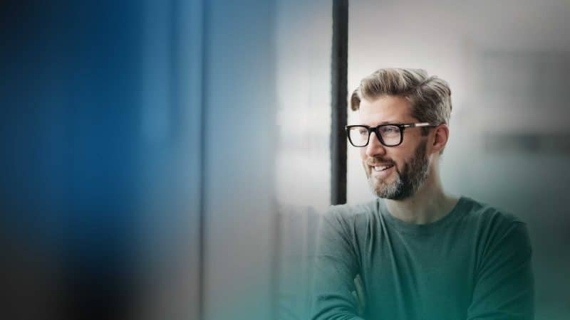 Ein Mann mit Bart und Brille sitzt in seinem Büro und schaut auf ein Gerät.