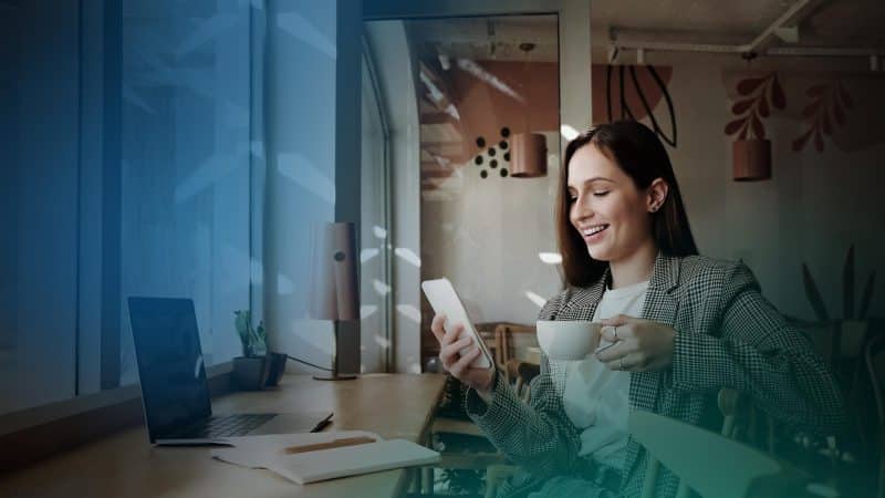 Eine Frau mit einer Tasse Kaffee in der Hand schaut auf ihr Smartphone